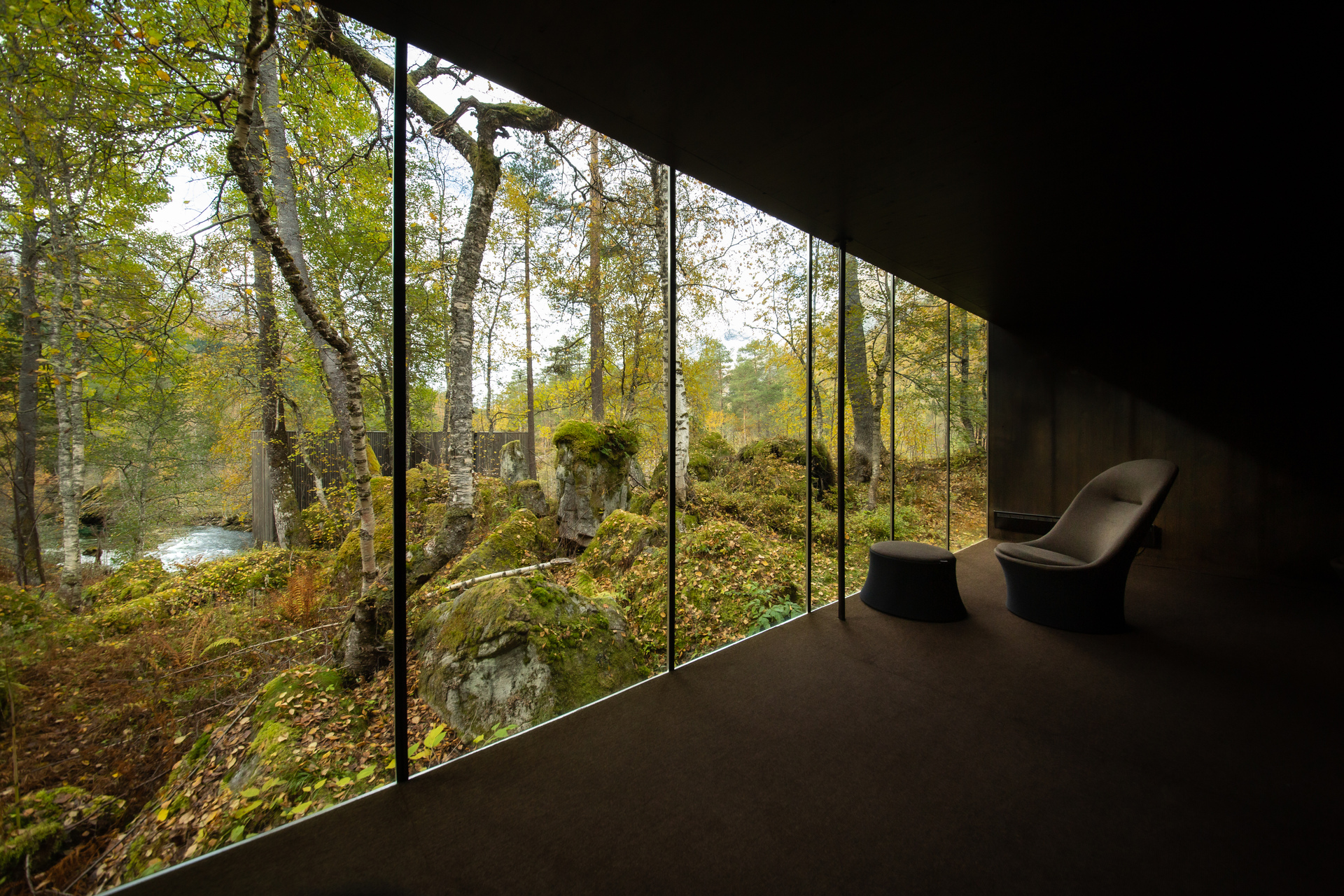 Mørkt rom med store vinduer og utsikt ut mot naturen